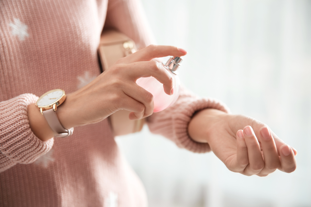 Closeup of a young woman putting on rose perfume 