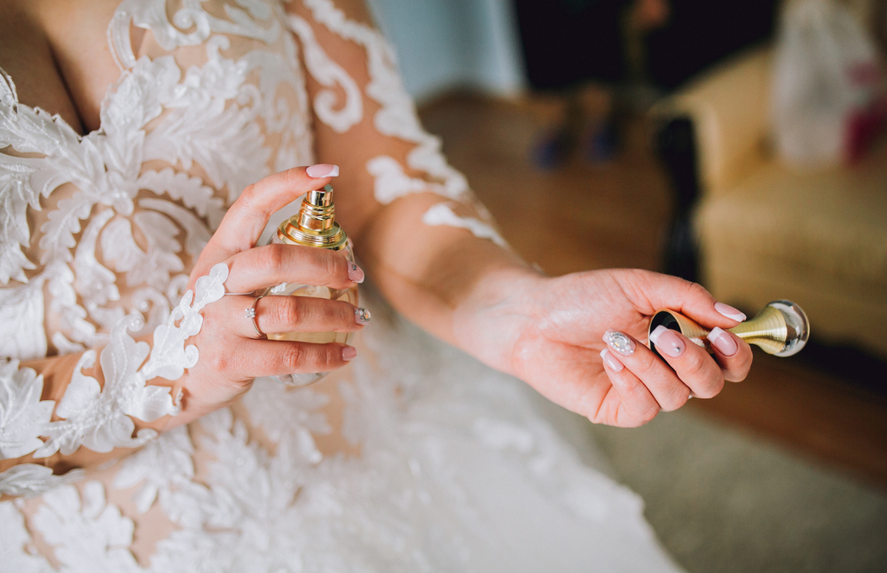 Bride in white gown putting on perfume