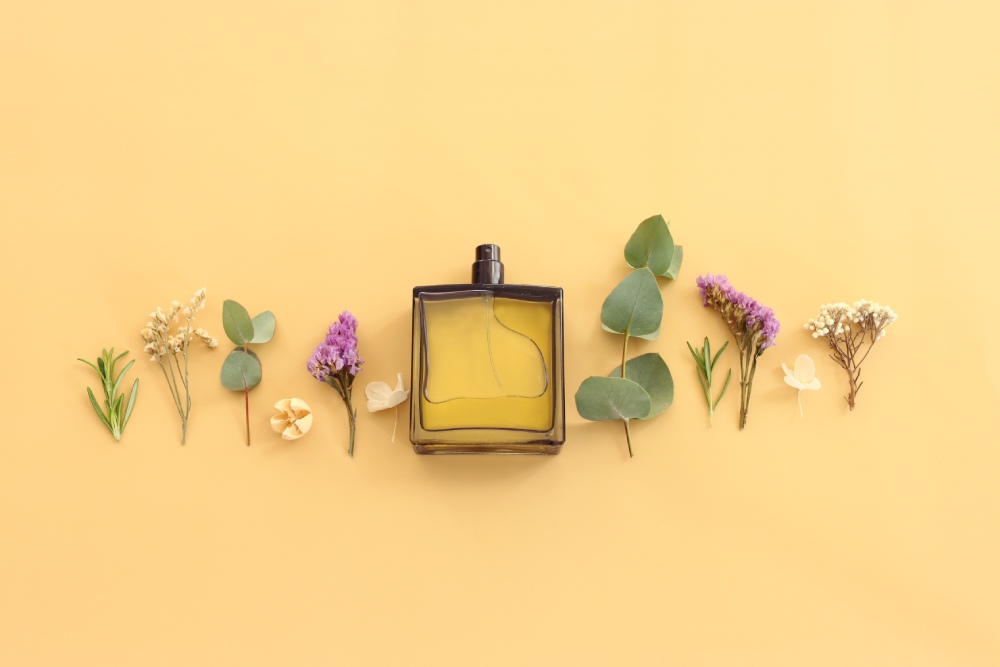 Top view of elegant perfume bottle with flowers and oud over yellow background.